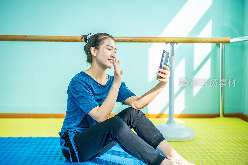 美丽的亚洲舞者在排练大厅使用智能手机