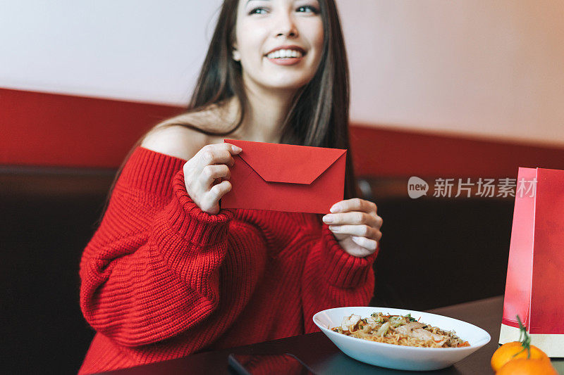 美丽年轻的亚洲女子在餐厅吃亚洲食物与红包庆祝中国新年