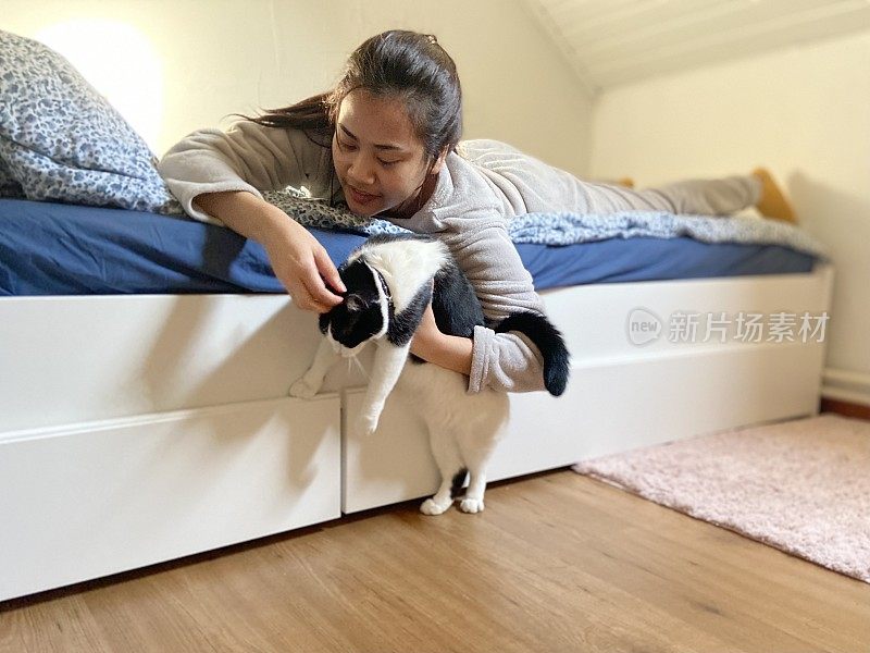 年轻的亚洲女人放松在卧室和猫