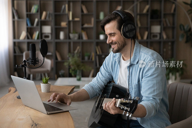 面带微笑的男人戴着耳机用着笔记本电脑，弹着原声吉他