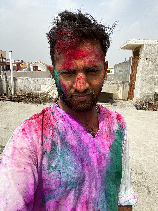 印度一名男子穿着库尔塔传统服装，身上涂满了油漆粉，在胡里节的色彩和爱漆大战中胡闹，微笑着看着镜头