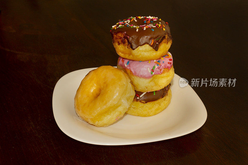 各种口味的甜甜圈草莓，巧克力和奶油，上面的彩色糖果组合在一个白色的盘子上。自制甜甜圈的照片。