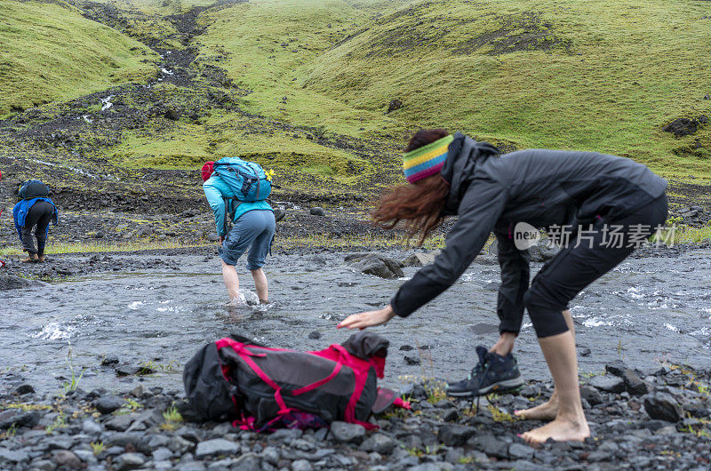 游客，男女在冰岛南部的黑色熔岩上穿过冰冷的河水