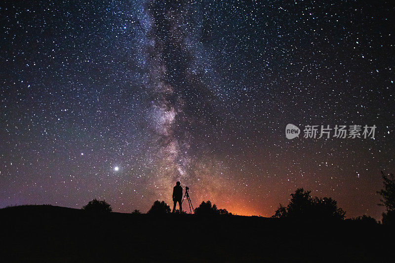 男人的剪影在黑暗的背景。摄影师拍摄的风景。相机三脚架。夏天的星空。星星在天空。美丽的夜晚景观。长时间的曝光。银河系。摘要深空