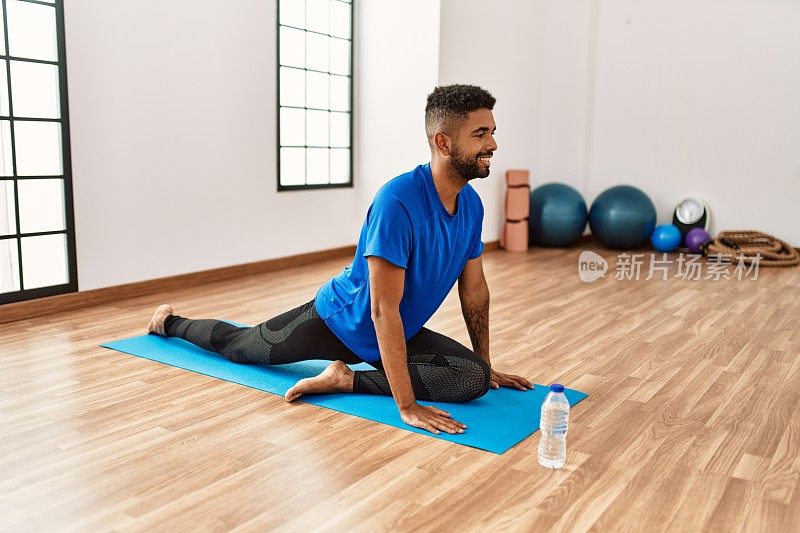 英俊的西班牙裔男子在瑜伽垫上做运动和伸展，在健身房练习柔韧性和训练
