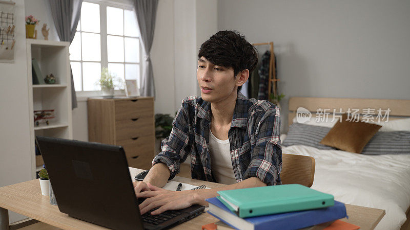 快乐的亚洲男性韩国学生在卧室的笔记本电脑上学习