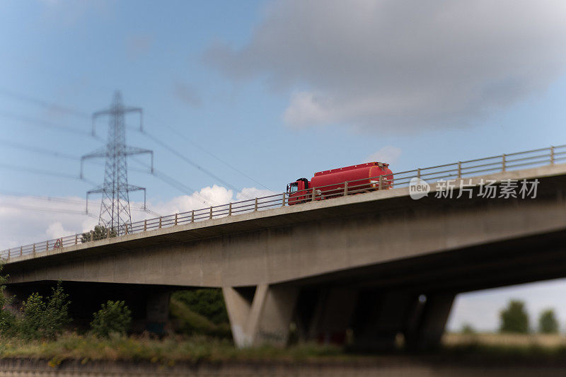 货物运输油罐车行驶在高速公路河桥上，有电站和电线的工业背景。用Lensbaby相机拍摄故意模糊