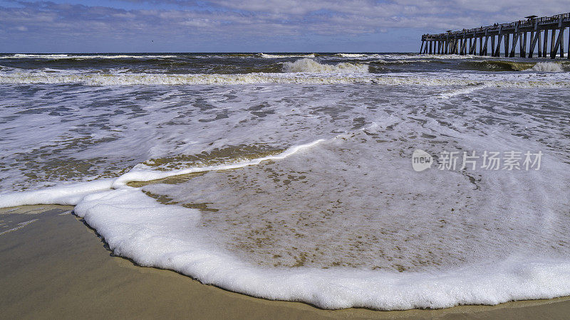 美国北佛罗里达州杰克逊维尔JAX海滩钓鱼码头下的海景，白色泡沫的海浪在白色沙滩上翻滚