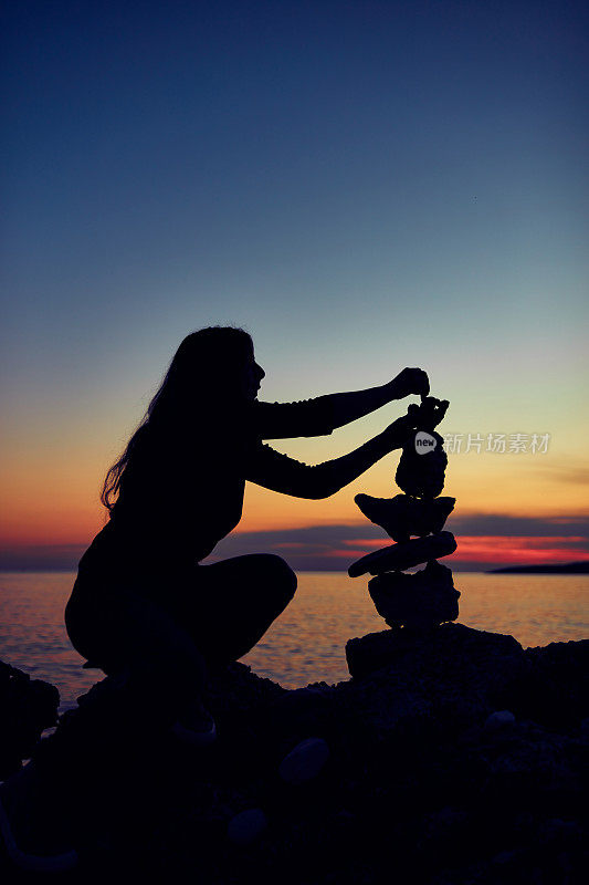 一个女人的剪影平衡岩石和石头上的海洋海岸在日落日出的时候。
