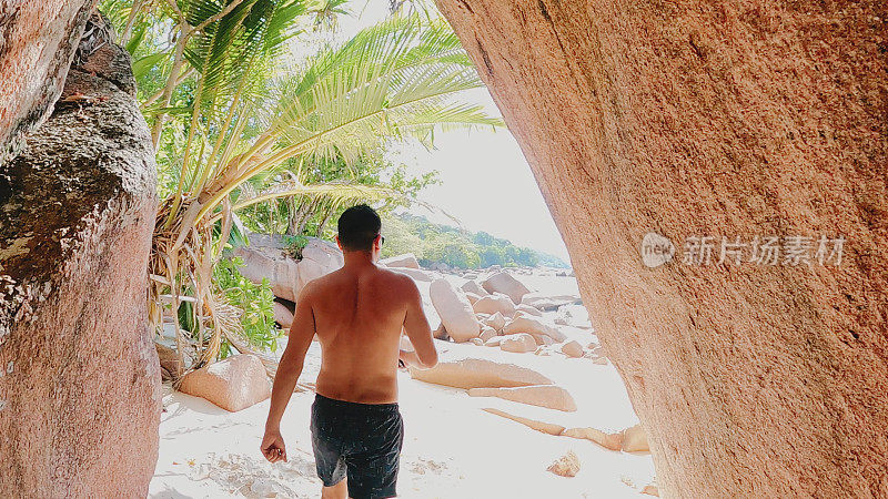 年轻人在异国情调的海滩上散步，海滩上有巨大的石头和棕榈树。
