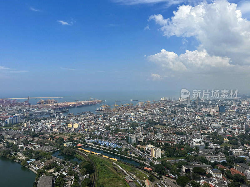 斯里兰卡科伦坡的城市景观图片，首都的摩天大楼，港口，道路，铁路轨道，港口起重机，蓝色多云的天空，重点在前景