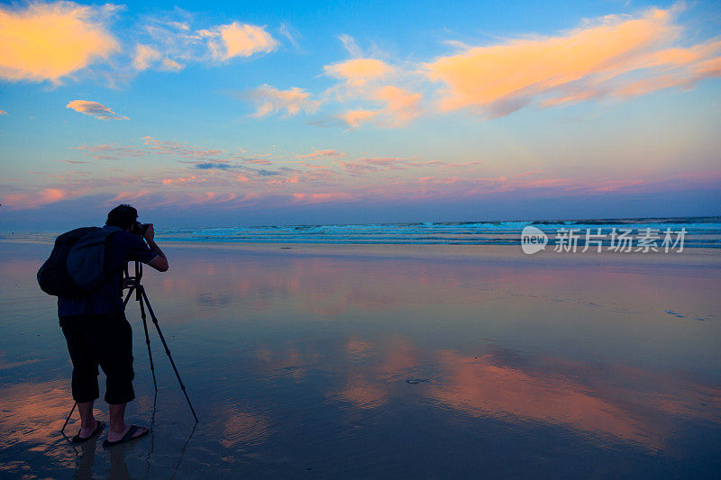摄影师在日落海滩与单反相机和三脚架
