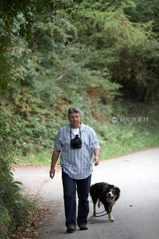 成熟的男人在乡村小路和边境牧羊犬