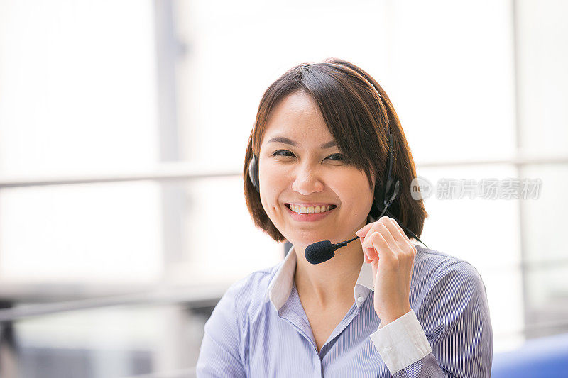 在办公室里用耳机说话的亚洲商务女性