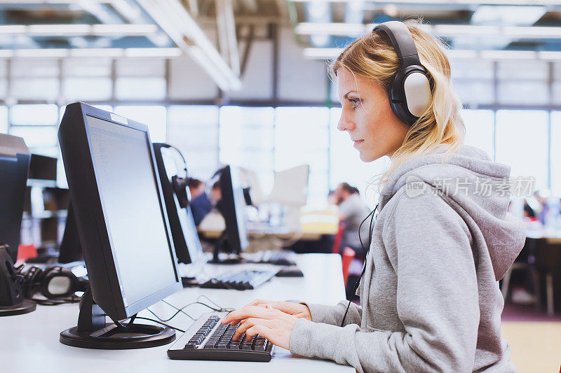 成人教育，学生戴着耳机在图书馆用电脑工作