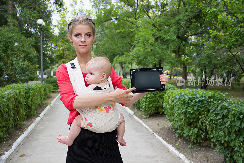 抱着婴儿的女人指着笔记本电脑的屏幕。