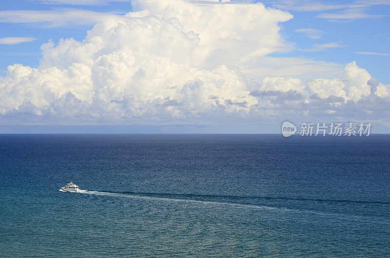 一艘游艇在云下航行在美丽的蓝色海洋上。