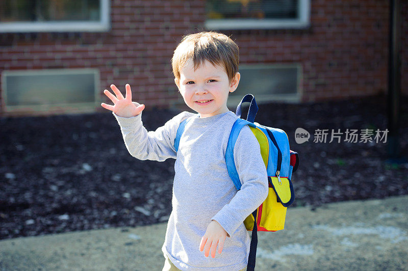 小男孩在上学的第一天穿着书包挥手