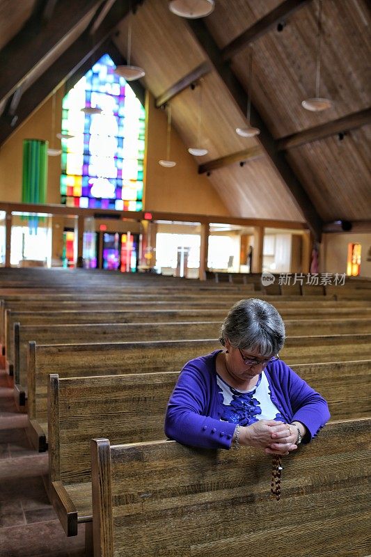 老妇人跪在天主教教堂的皮尤祈祷