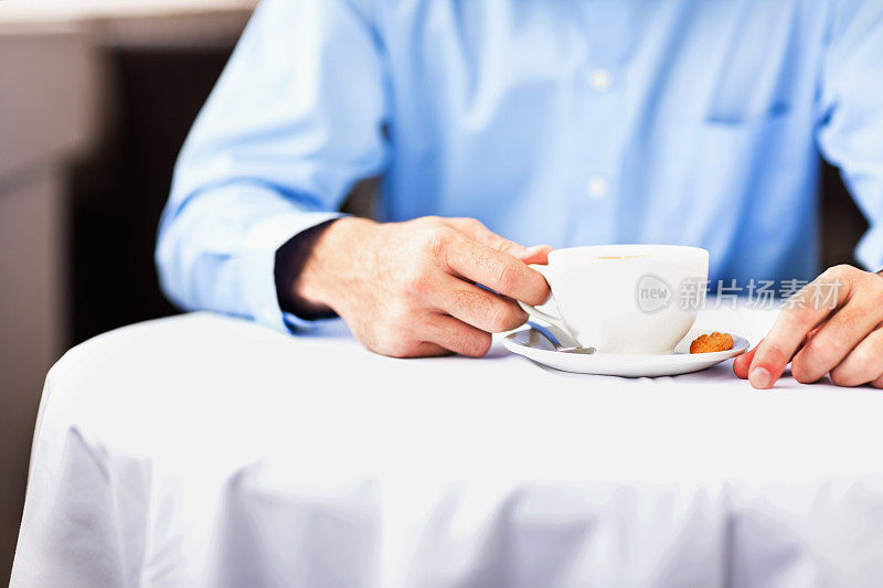 拿着咖啡杯坐在餐厅桌子旁的男人