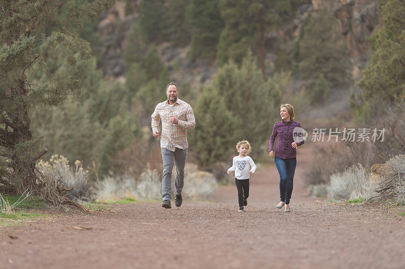 一对现代夫妇带着他们的小女儿在自然小道上跑步
