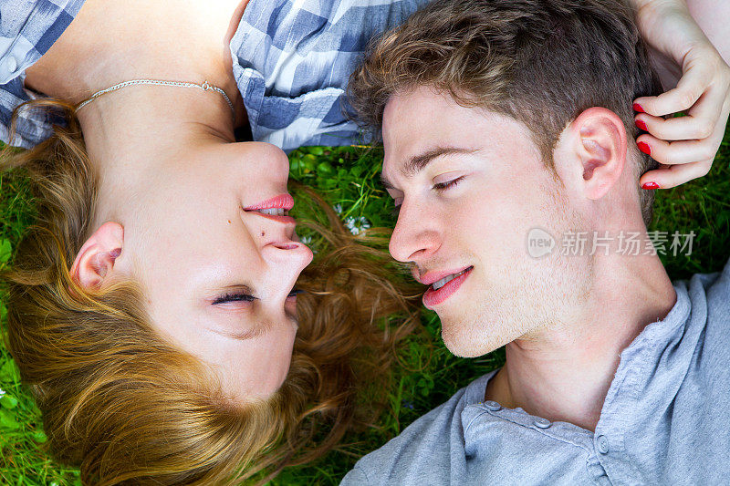一对美丽的年轻夫妇躺在草地上看着对方