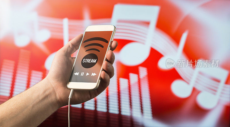 现代在线音乐流媒体概念。近距离的一个人拿着智能手机在手里和听音乐的移动应用程序。红色模糊的笔记背景。