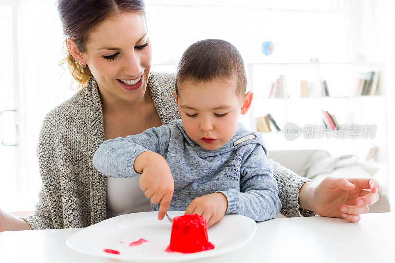 年轻漂亮的妈妈和她的儿子在家里吃草莓果冻。