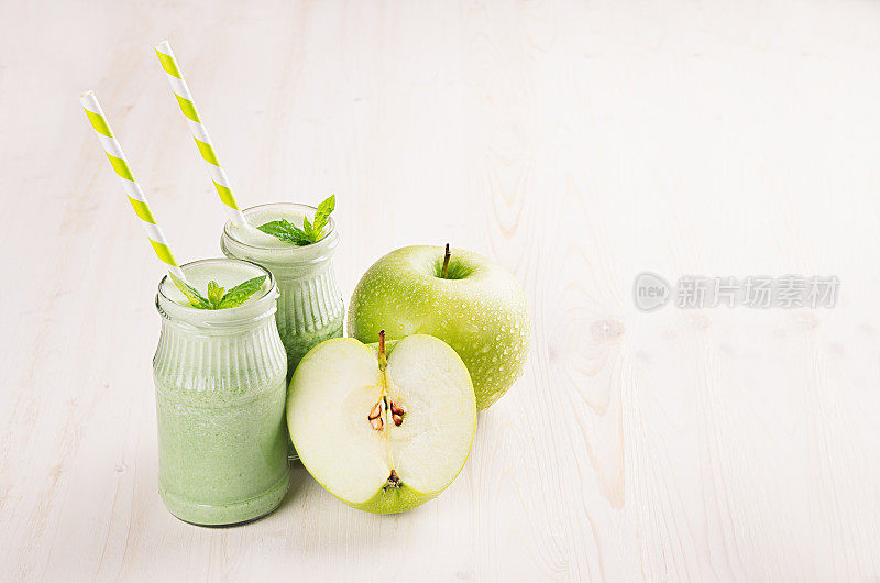 新鲜混合青苹果水果冰沙与吸管，薄荷叶，苹果。白色木板背景，复制空间。