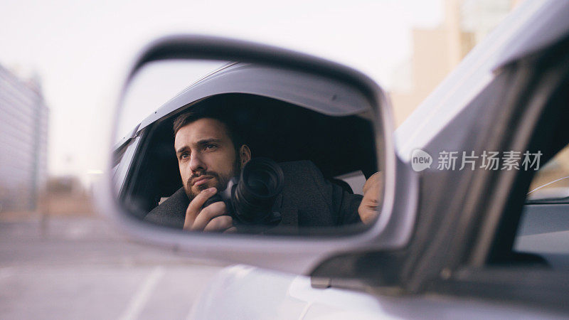 侧面镜中反映的年轻私家侦探坐在车内，用单反相机拍照