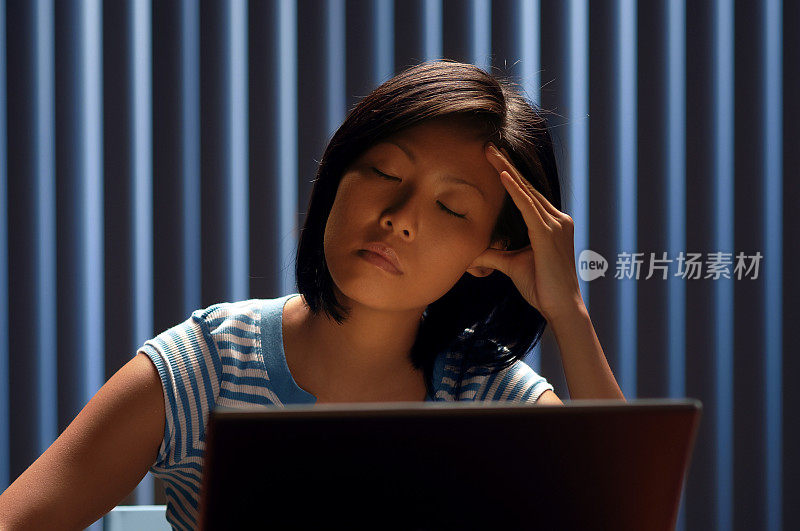年轻的亚洲女人用笔记本电脑揉太阳穴