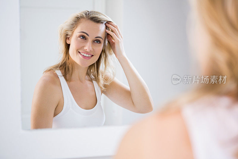 一名年轻女子在浴室镜子前检查头发