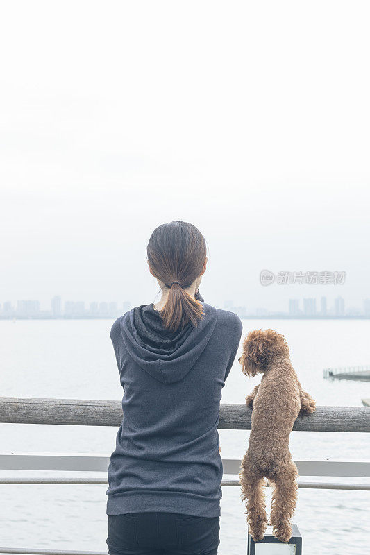 后视图的女人和可爱的小狗靠在栏杆上看风景