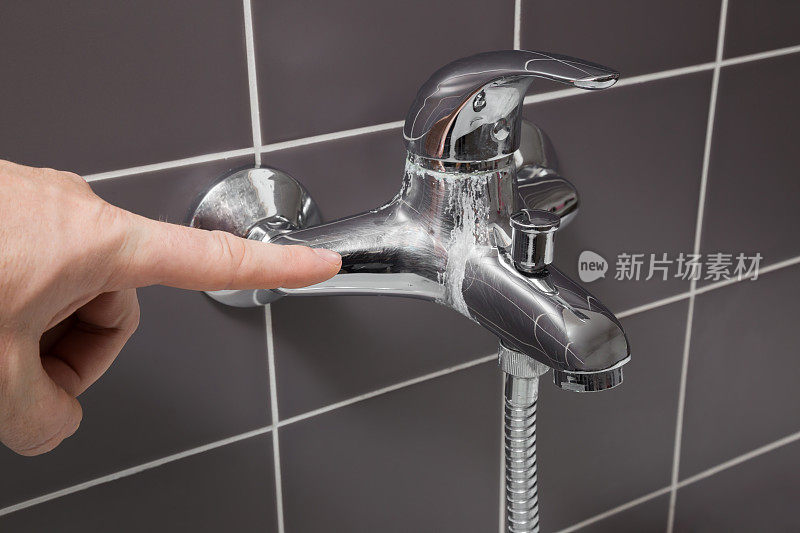 男人的手指指着浴室里钙化的水龙头。问题的概念。