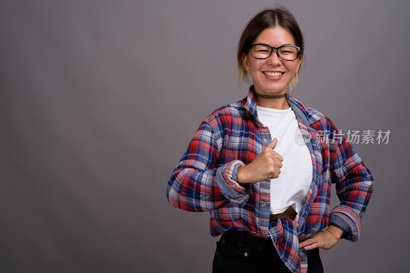 工作室拍摄的年轻亚洲妇女穿着格子衬衫，以灰色背景