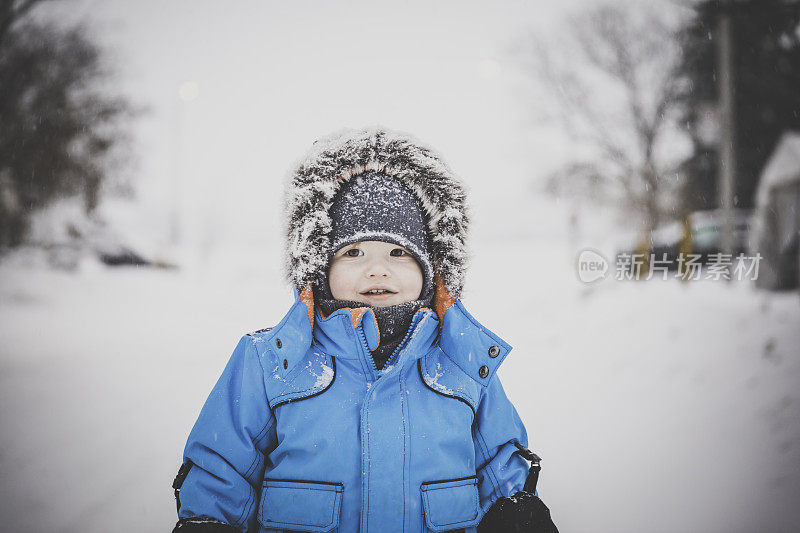 穿着蓝色冬装的小男孩和雪玩