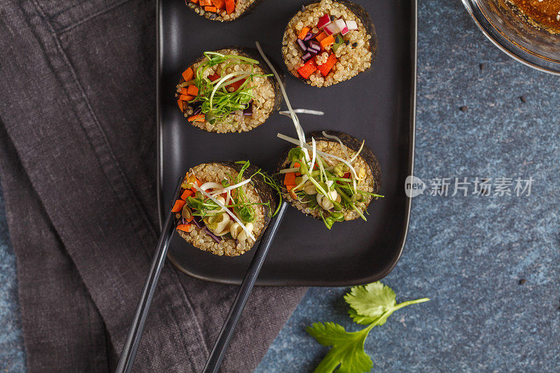 纯素寿司卷配藜麦、蔬菜和豆瓣酱在黑色的盘子上，黑色的背景。前视图。素食健康食品概念。