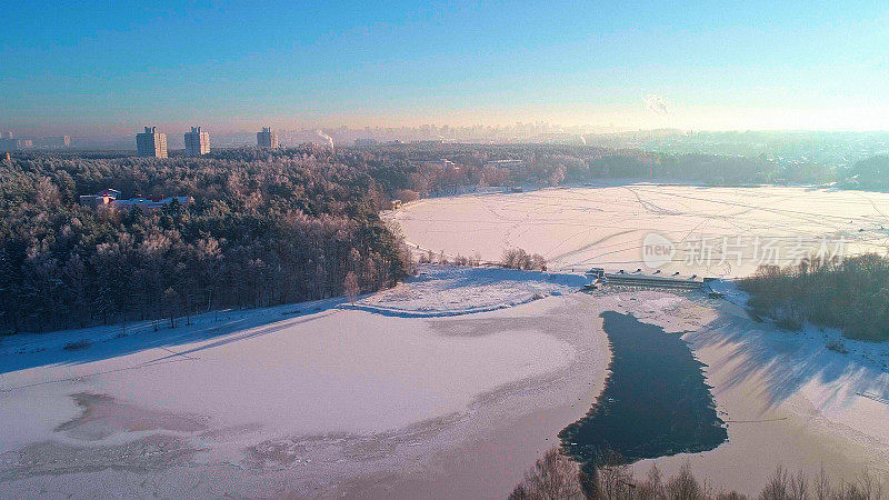 从空中俯瞰日落时冰冻的河流和森林的城市全景。