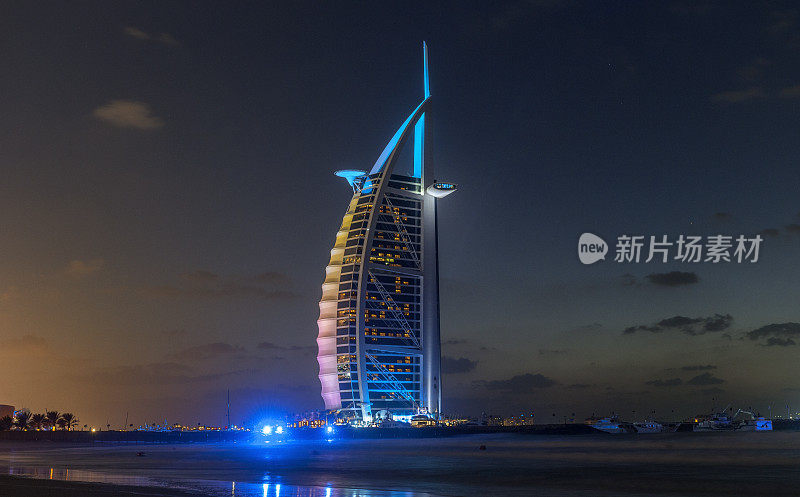 阿拉伯联合酋长国迪拜。从朱美拉海滩上的迪拜帆船酒店的夜景。阿拉伯塔是迪拜的地标之一，也是世界上最豪华的酒店之一