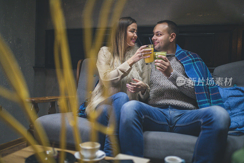 真爱。一对快乐浪漫的夫妇坐在舒适的格子图案下的沙发上，微笑着。他们穿着休闲服喝酒。