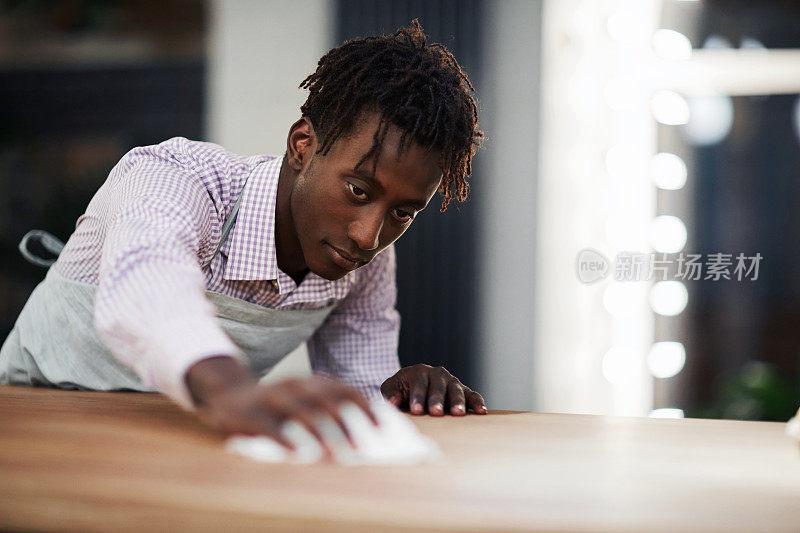 严肃专注的年轻非洲裔美国服务员，带着脏东西擦拭桌子，检查桌子表面的清洁