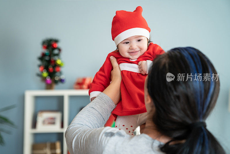 婴儿女孩的肖像在圣诞老人的服装凝视妈妈的肩膀