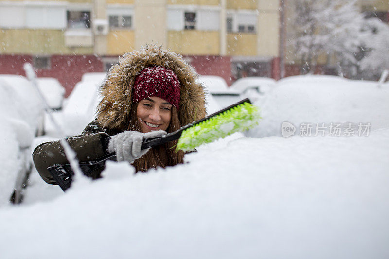 年轻女子在清理车上的积雪