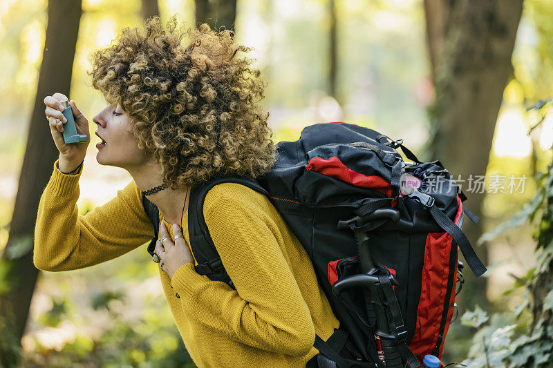 在树林里使用吸入器的女性徒步旅行者。年轻女性用吸入器治疗哮喘