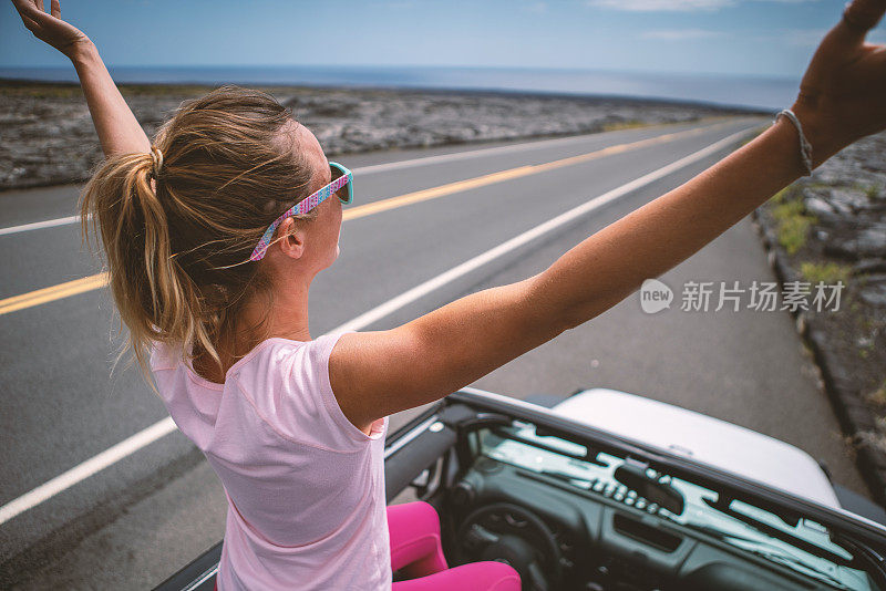 年轻女子坐在4x4汽车上，双臂伸开享受公路旅行