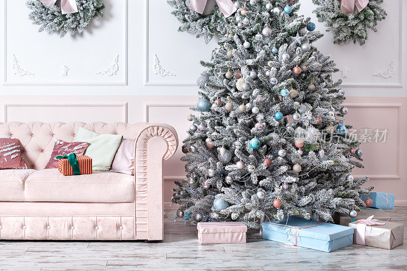 豪华客厅内饰以沙发装饰别致的圣诞树、礼物和枕头。经典的粉红色内饰。圣诞节在家里。圣诞树背景上的粉色沙发。明信片模板