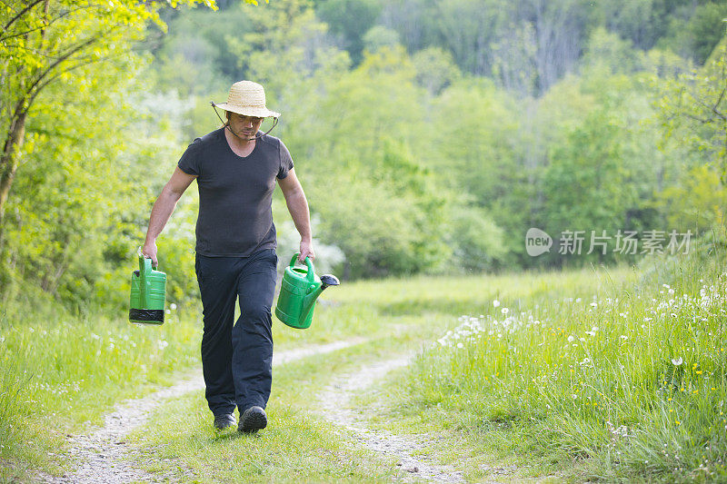 农民扛着水罐在土路上的乡村场景