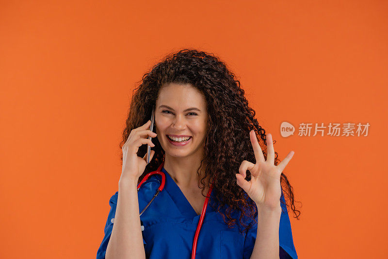 年轻女医生使用智能手机，显示OK标志，橙色背景