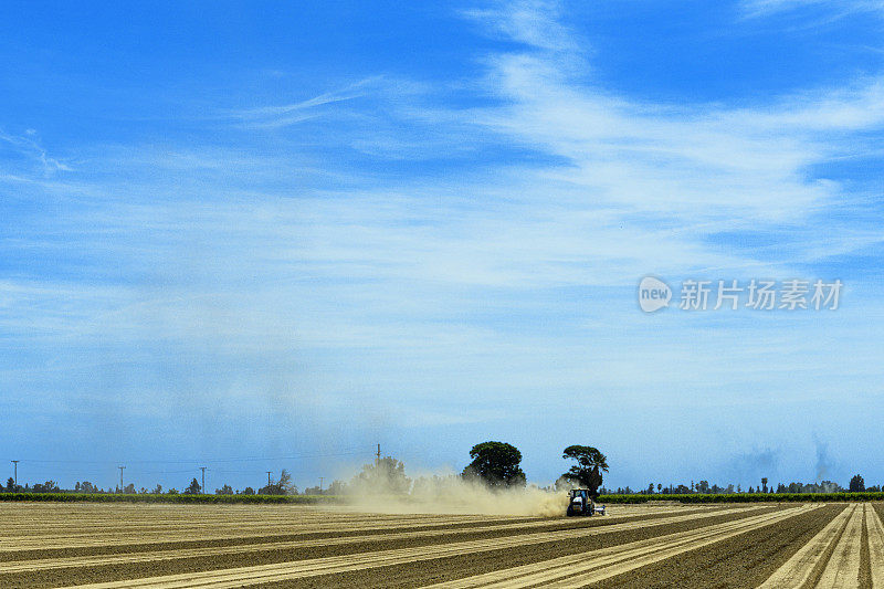 多云的天空下，拖拉机在尘土飞扬的田野上犁地