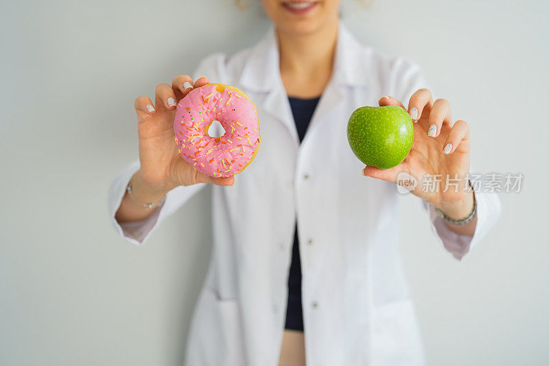 女性健康营养师手里拿着甜甜圈和苹果。健康饮食生活